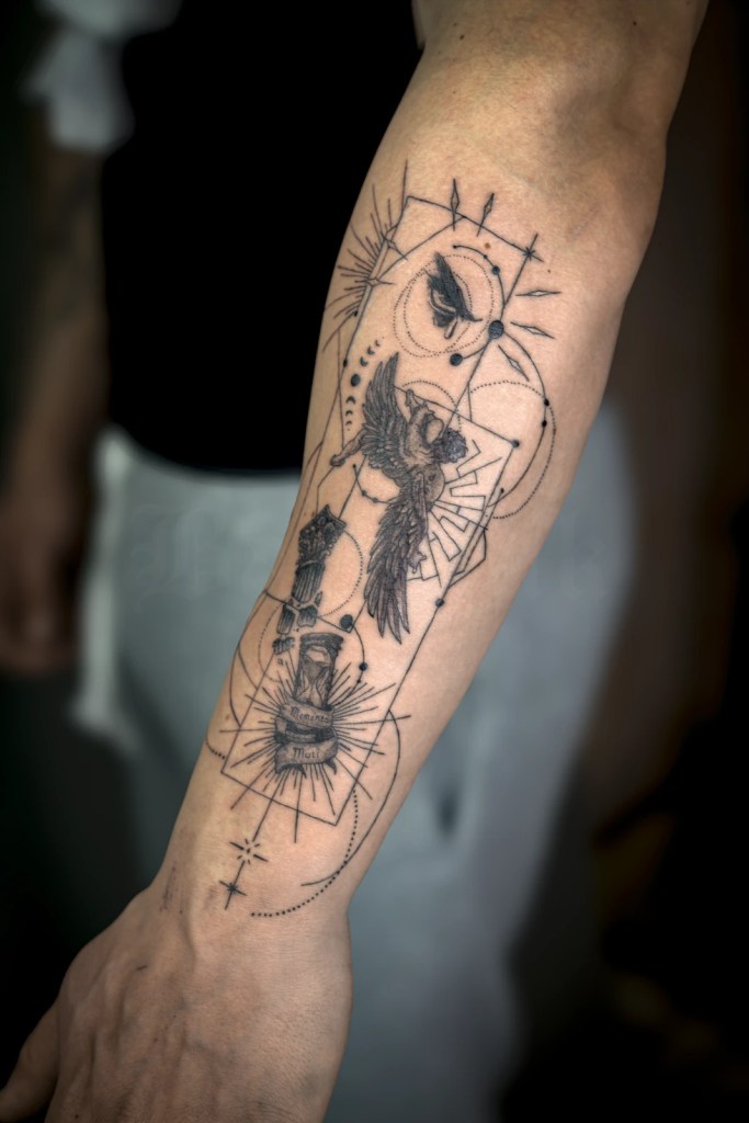 Tatouage noir et gris sur l’avant-bras mêlant oiseau aux ailes déployées, motifs célestes et tracés géométriques