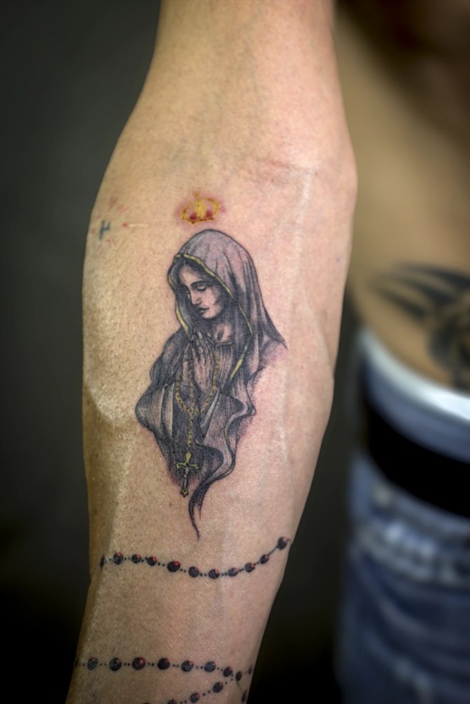 Portrait de femme voilée et chapelet tatoués sur l’avant-bras