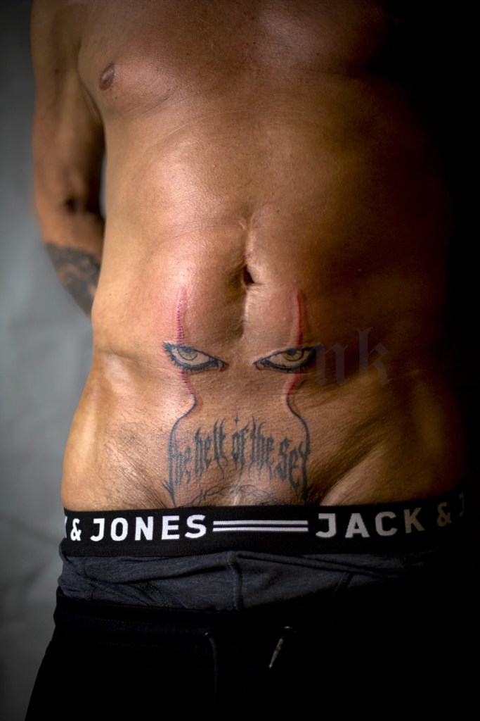 Tatouage de regard et de lignes rouges sur le ventre, au-dessus d’un lettrage noir