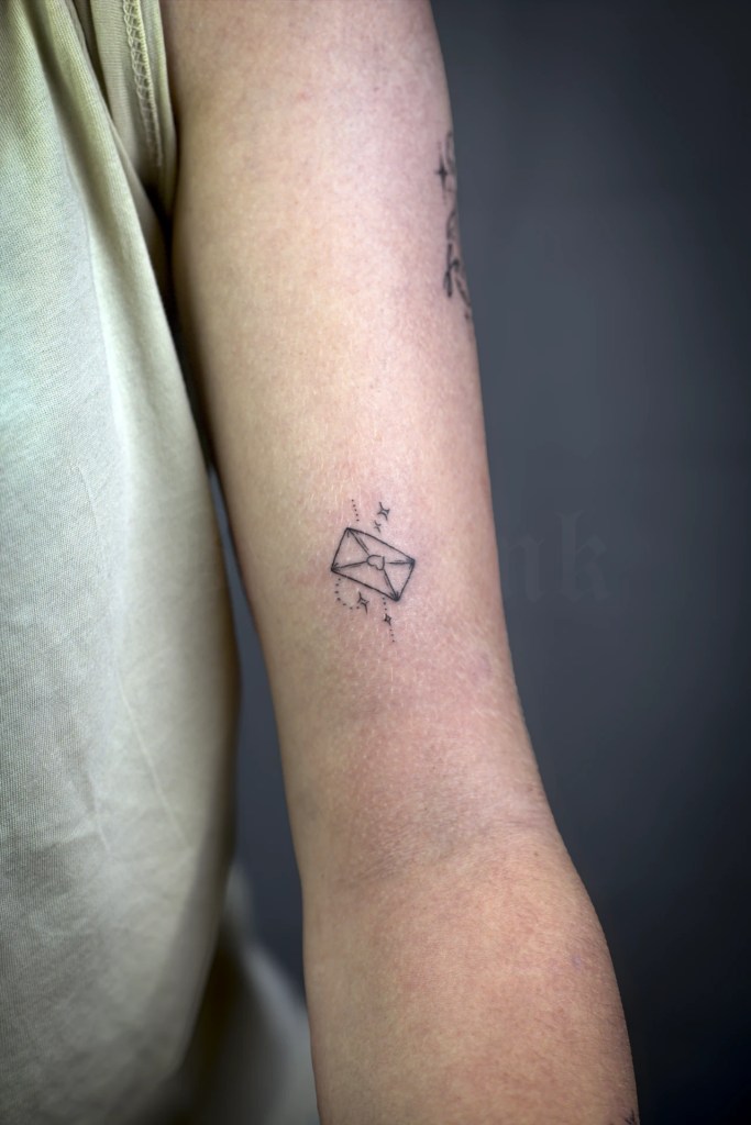 Petit tatouage d’enveloppe entourée d’étoiles sur le bras