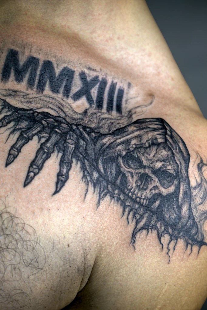 Crâne encapuchonné et main squelettique tatoués sur le haut du torse