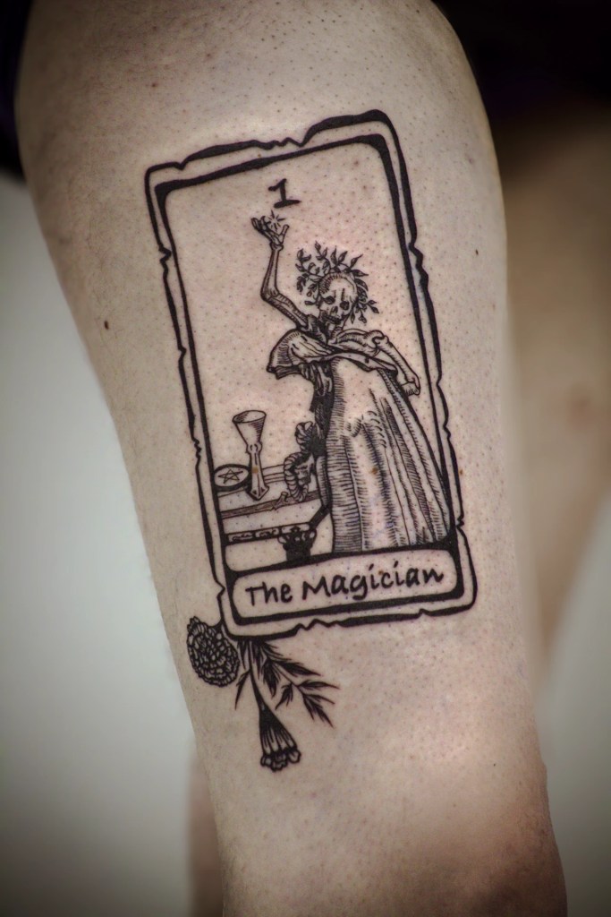 Tatouage de carte de tarot The Magician, avec personnage squelettique et fleurs dans un style gravure noire