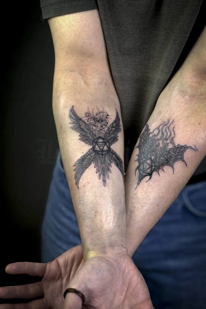Deux tatouages de dés à vingt faces sur les avant-bras, avec ailes angéliques et ailes démoniaques