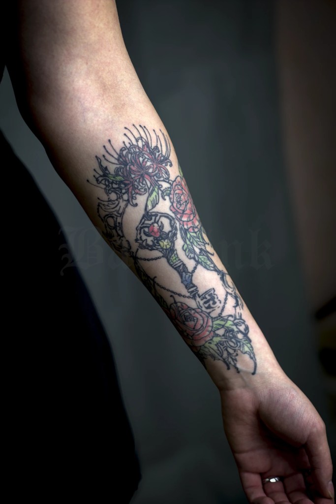 Composition florale sur l’avant-bras avec fleurs rouges et roses, feuillages verts et contours noirs